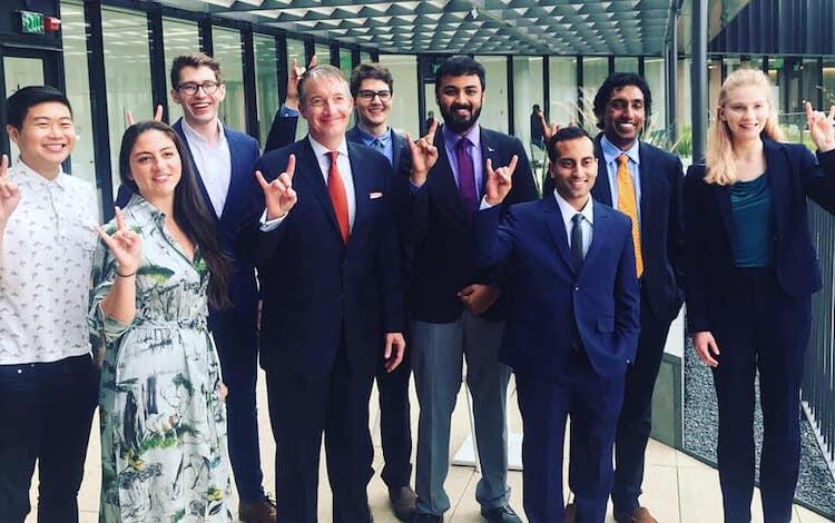 Group of 9 students in formal outfits holding up sign of the horns on their hands